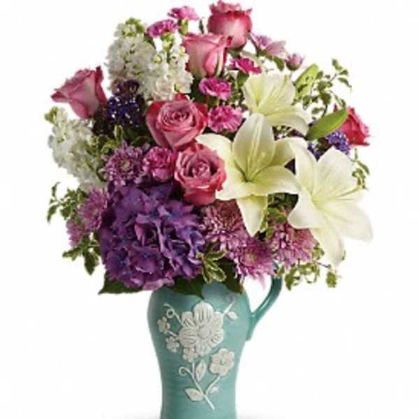 Mixed bouquet of pink, purple, and white flowers in a teal vase
