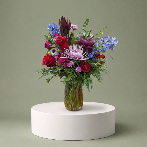 Mixed bouquet of red, purple, and blue flowers in a glass vase