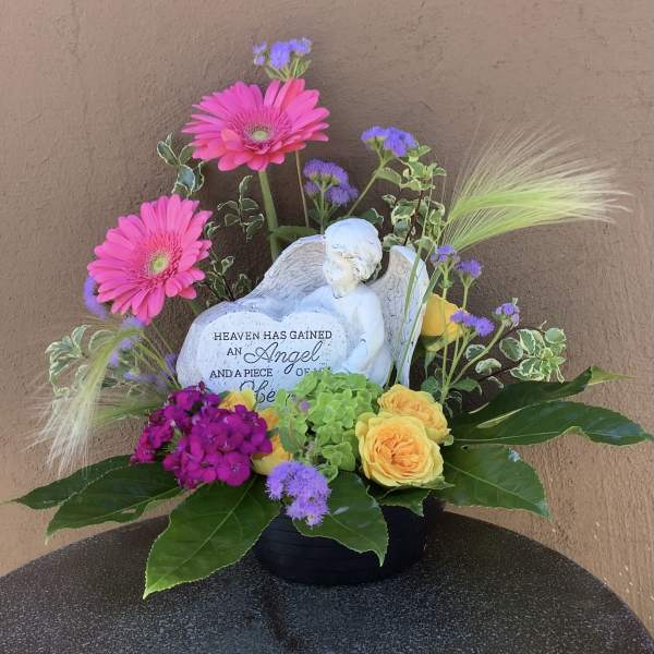 Floral sympathy arrangement with pink gerbera daisies and yellow roses around an angel figurine