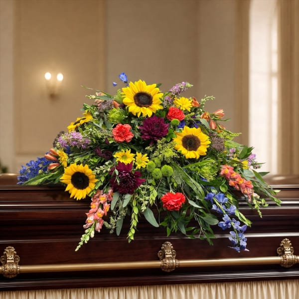 Large floral spray on a dark casket with sunflowers and mixed blooms