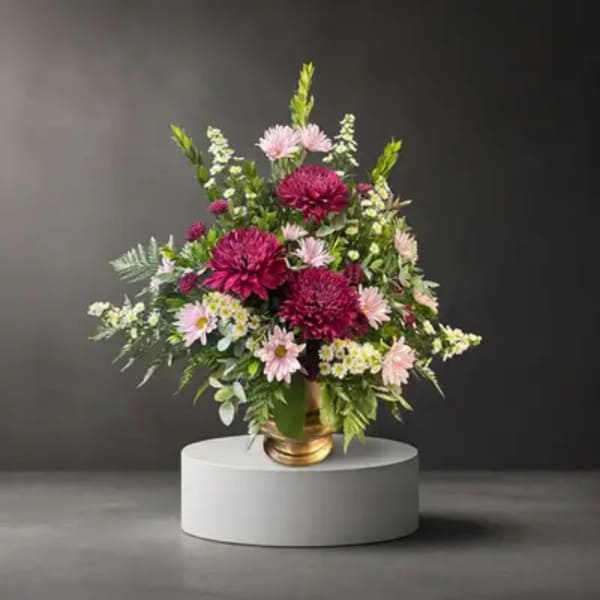 Pink and white flower arrangement in a gold vase on a pedestal