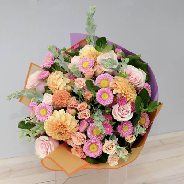Bouquet of pink and peach flowers wrapped in orange and purple paper