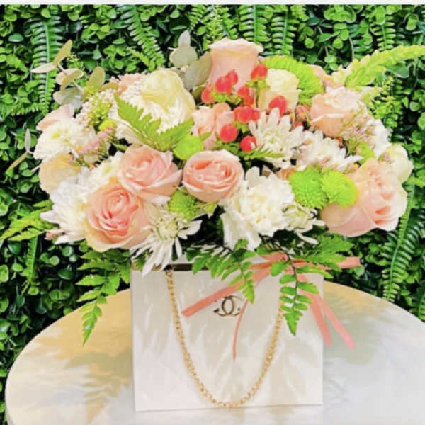 Pink and white rose arrangement in a white gift bag with ribbon