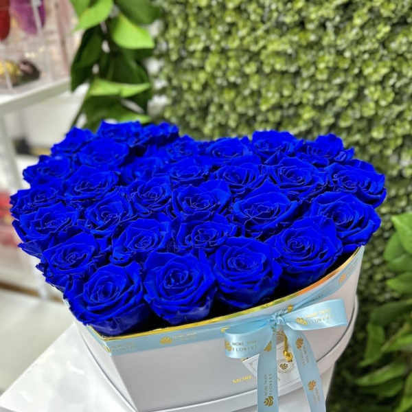 Heart-shaped box of vivid blue roses with a ribbon on a white pedestal