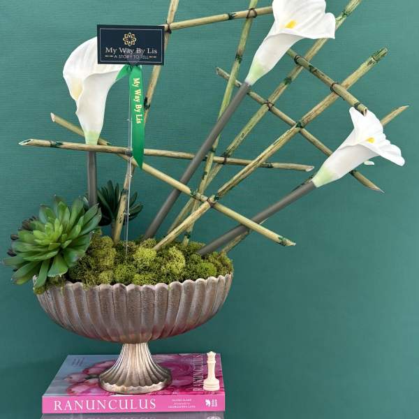 White calla lilies in a decorative pedestal bowl with succulents and bamboo stems
