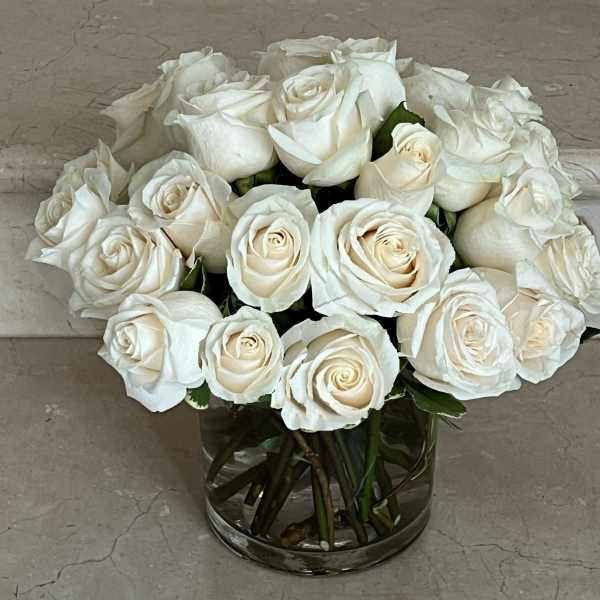 Compact arrangement of ivory white roses in a clear glass cylinder vase