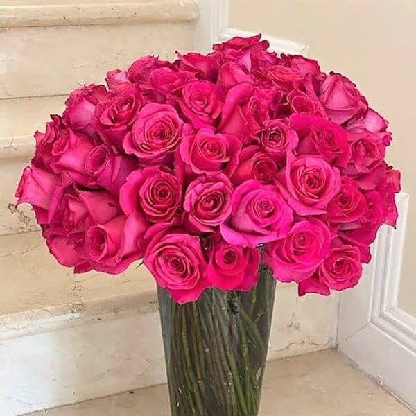 Tall clear glass vase filled with many hot pink roses on a stone step