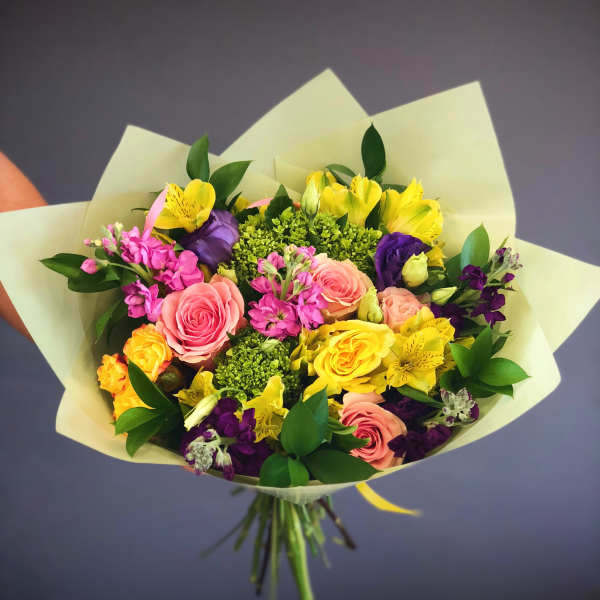 Mixed bouquet of pink, yellow, purple, and green flowers wrapped in pale paper