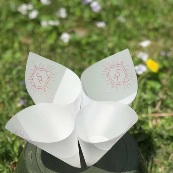 Four white paper cone holders with pink monogram marks on a dark base