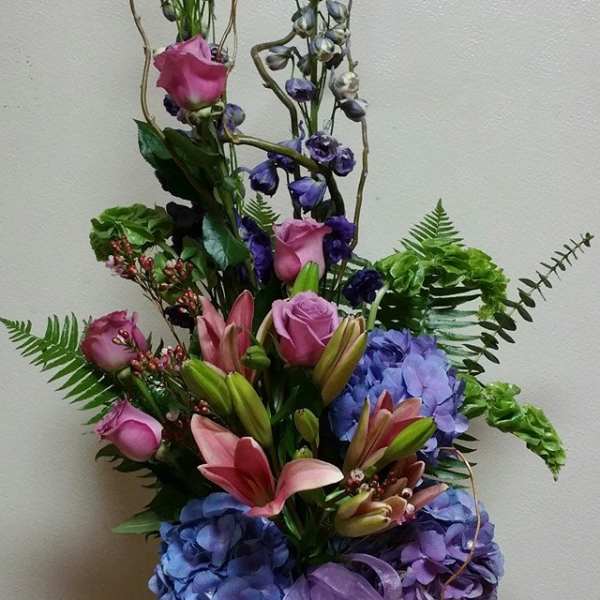 Tall bouquet of pink lilies, roses, and blue hydrangeas in a glass vase