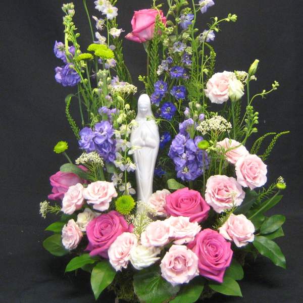 Tall floral arrangement with pink and purple roses around a white statue