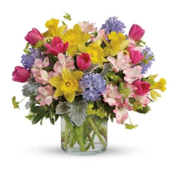 Mixed bouquet of pink, yellow, and lavender flowers in a clear glass vase