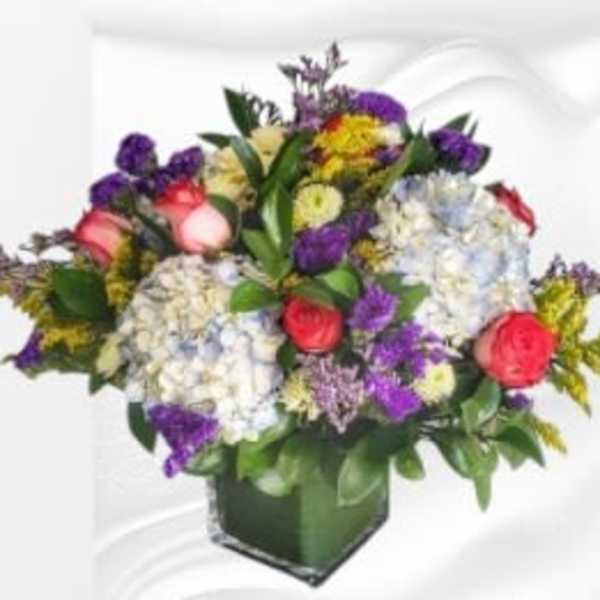 Mixed bouquet of roses, hydrangeas, and purple flowers in a square vase
