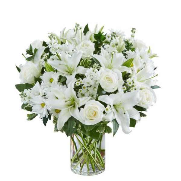 White lilies, roses, and daisies arranged in a clear glass cylinder vase