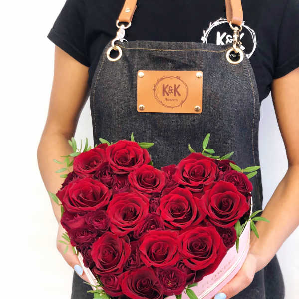 Heart-shaped box of red roses held by a person in an apron
