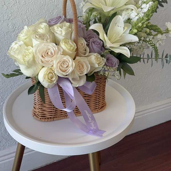 Basket of cream and lavender roses with white lilies and ribbon