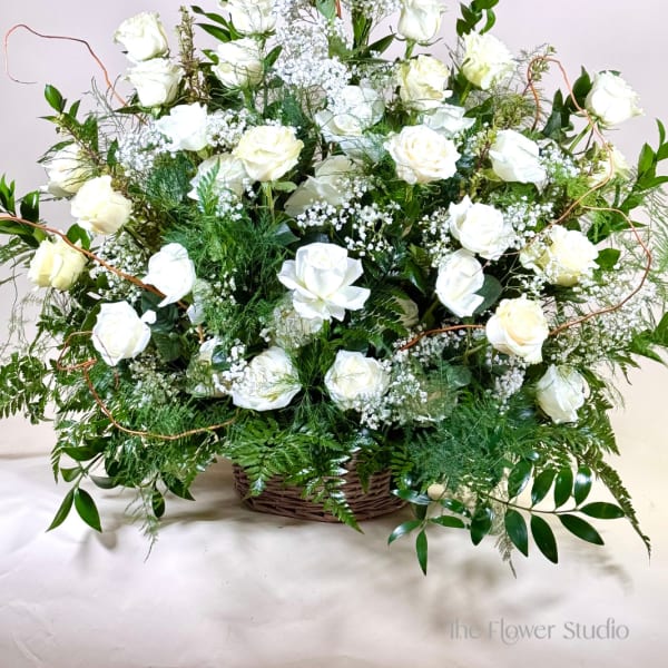 Large white rose arrangement in a wicker basket with greenery