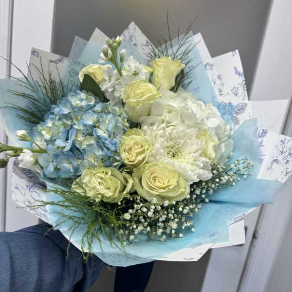 Bouquet of pale yellow roses, blue hydrangeas, and white flowers wrapped in blue paper