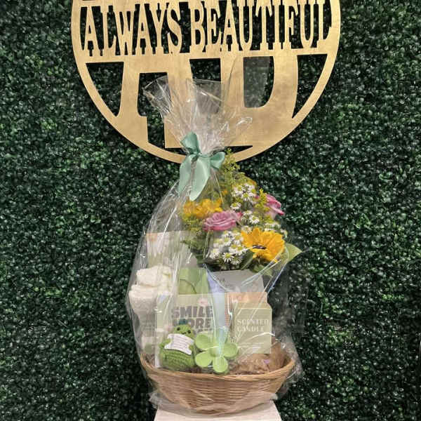 Gift basket with flowers, candles, and a plush toy under clear wrap