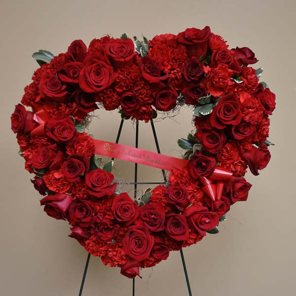 Heart-shaped red rose wreath on a stand with a ribbon