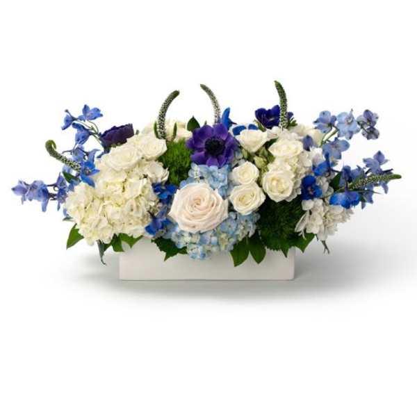 Low centerpiece of white and blue flowers, including roses and hydrangeas, in a rectangular white container