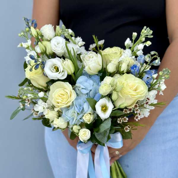 Handheld bouquet of white and pale yellow flowers with blue accents and ribbon