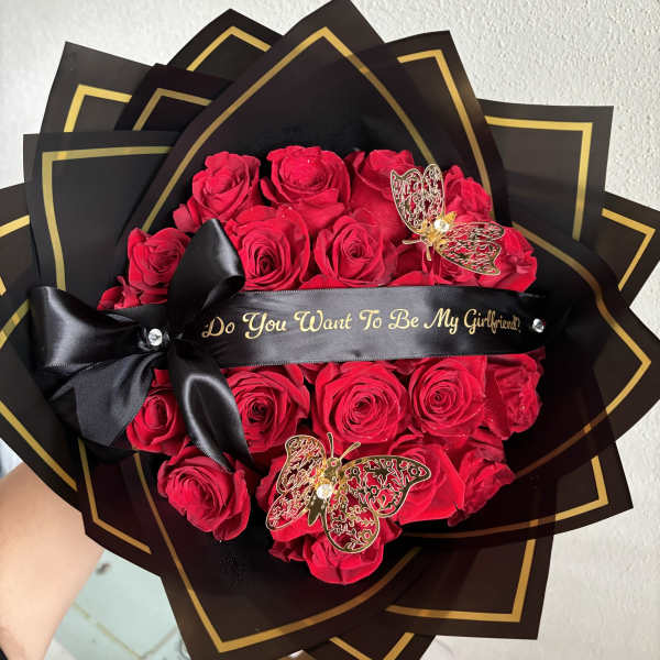 Red roses wrapped in black paper with gold trim and a black ribbon