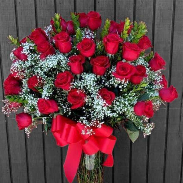Bouquet of red roses with baby's breath in a glass vase and red ribbon