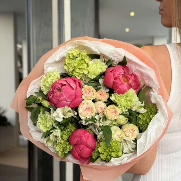 Bouquet of pink peonies and green hydrangeas wrapped in peach paper