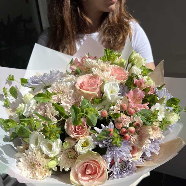 Large pastel bouquet of roses, chrysanthemums, and white blooms wrapped in paper