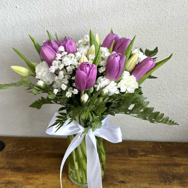 Bouquet of purple tulips and white flowers in a glass vase with a white ribbon