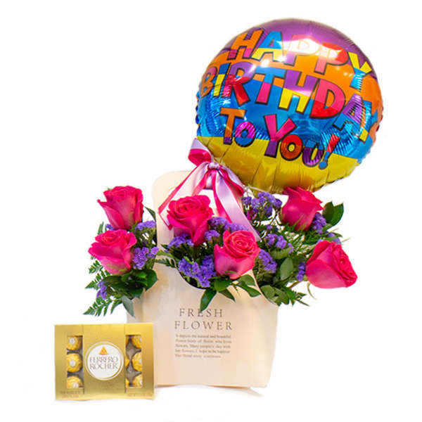 Pink roses in a gift bag with a birthday balloon and chocolates