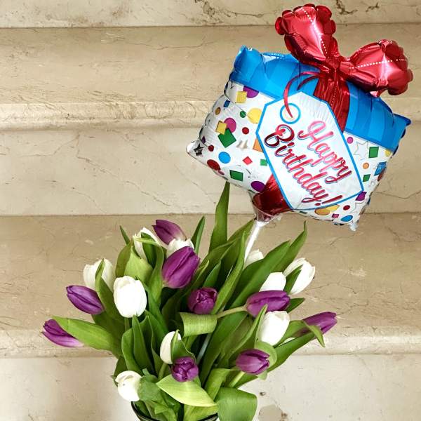 Purple and white tulips in a glass vase with a birthday balloon