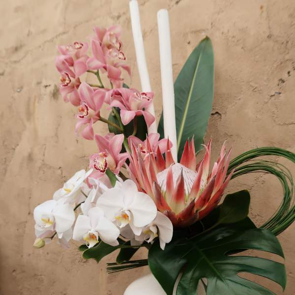 Pink and white orchids with a protea in a white vase