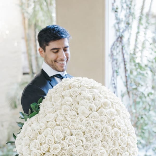 Man holding a large round bouquet of white roses