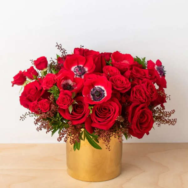 Red roses and red anemones arranged in a gold vase