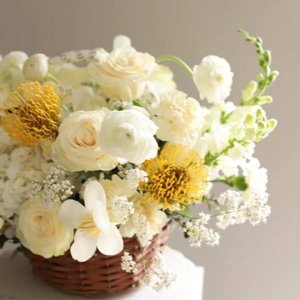 White floral arrangement in a wicker basket with yellow accents