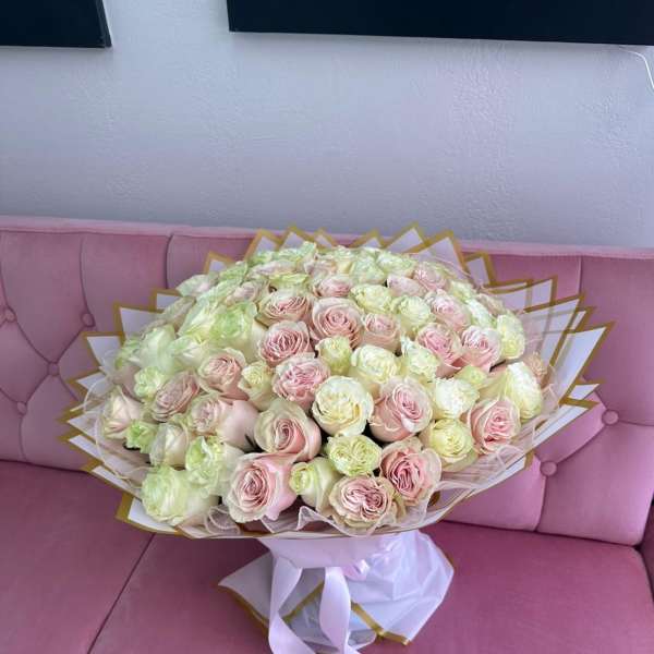 Large bouquet of pale pink and cream roses wrapped in white paper with gold trim