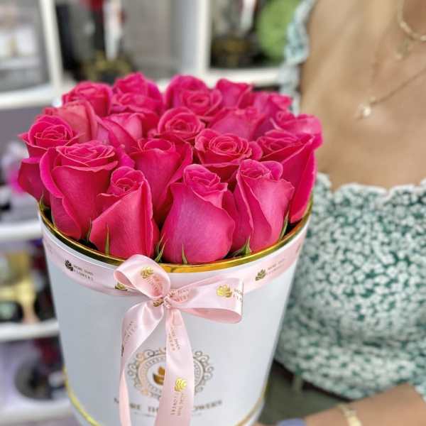 Round box filled with bright pink roses tied with a pink ribbon