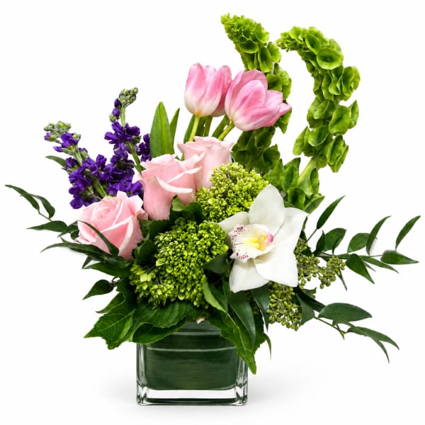 Pink roses, tulips, and a white orchid in a glass vase with purple blooms
