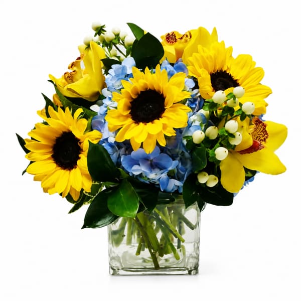 Bouquet of sunflowers, blue hydrangeas, and yellow orchids in a glass vase