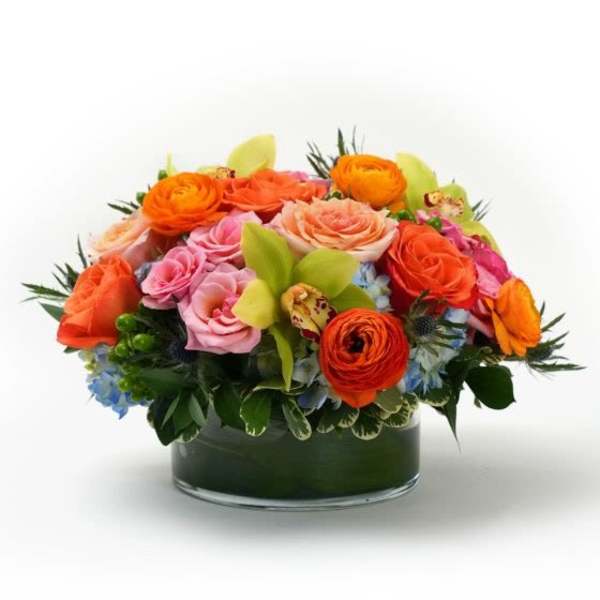 Low arrangement of orange and pink roses with green orchids in a clear glass cylinder vase
