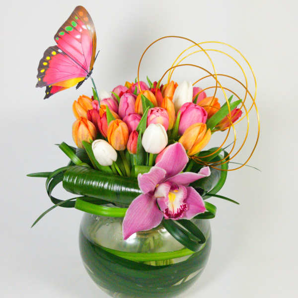 Tulip arrangement in a glass bowl with a pink orchid and butterfly decoration