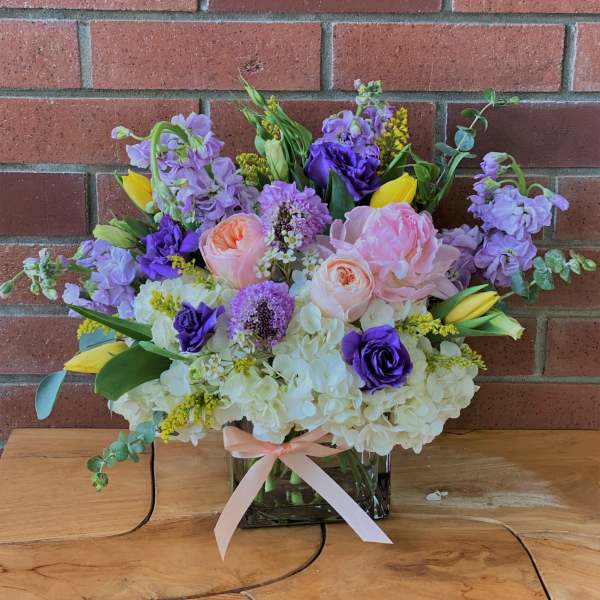 Bouquet of pink, purple, and yellow flowers in a glass vase with a ribbon