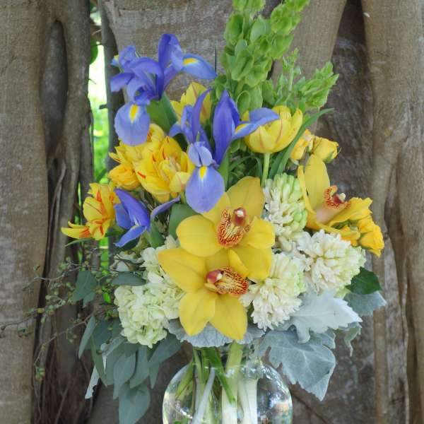 Bouquet of yellow orchids, blue irises, and white blooms in a glass vase