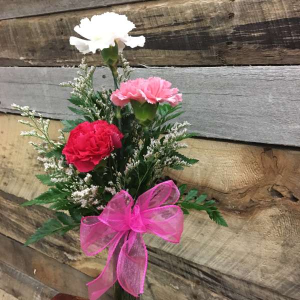 Small bouquet of carnations in a clear glass vase with a pink ribbon