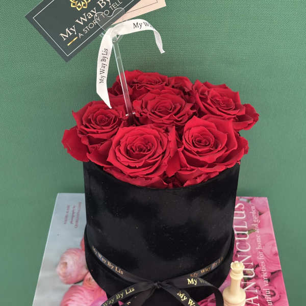 Red roses arranged in a black round box with a ribbon and card