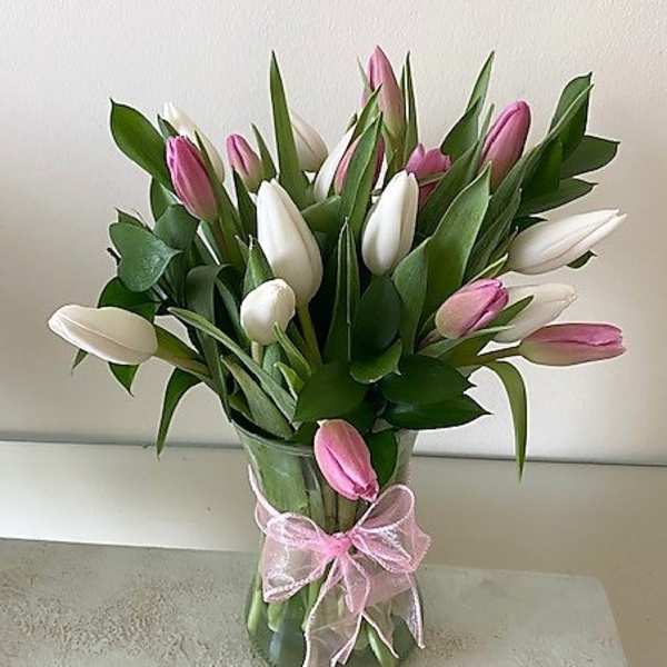 Pink and white tulips arranged in a clear glass vase tied with a pink ribbon bow