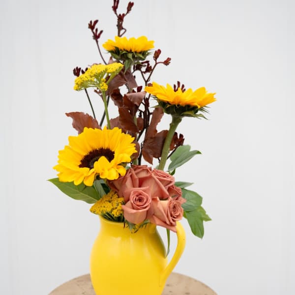 Yellow sunflowers and peach roses in a yellow pitcher vase