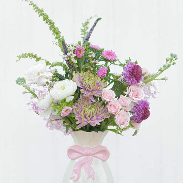 Pink and white mixed flower arrangement in a white vase with a pink bow